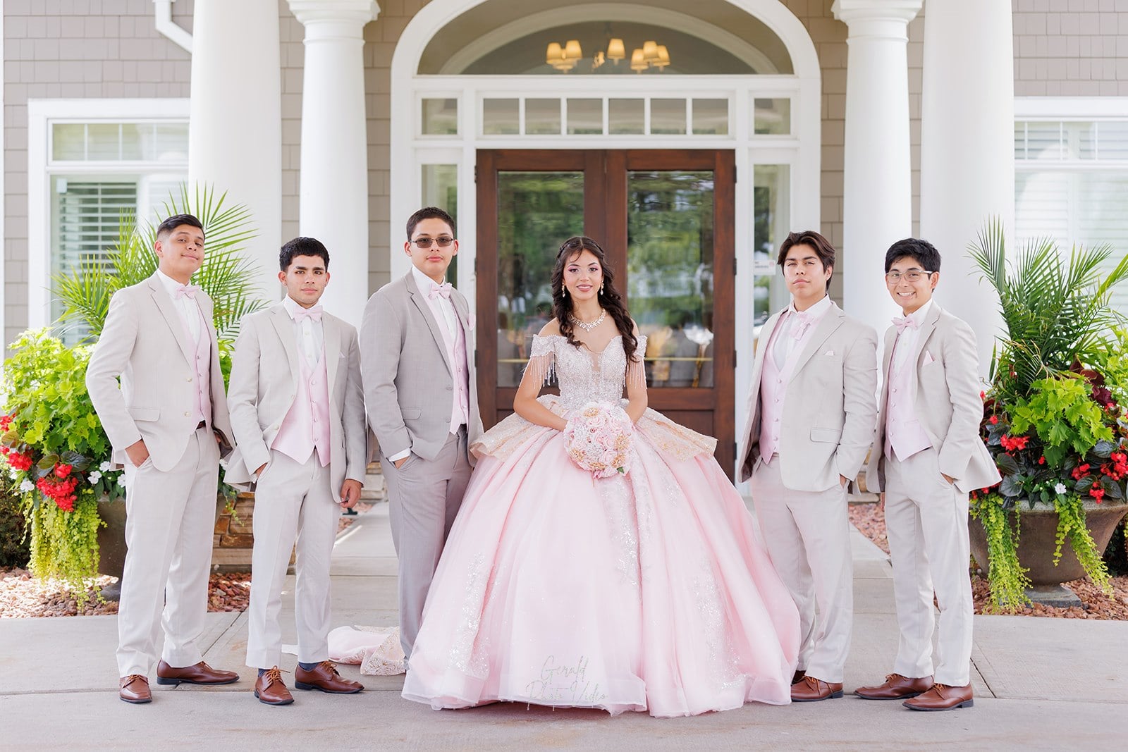 Quinceañera with her court of chambelanes in tan suits and pink bow ties at the Glen Oaks Country Club entrance in West Des Moines, Iowa
